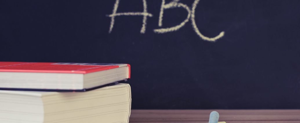 Stack of books and chalk on desk with ABC on blackboard background.