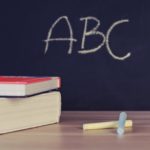Stack of books and chalk on desk with ABC on blackboard background.