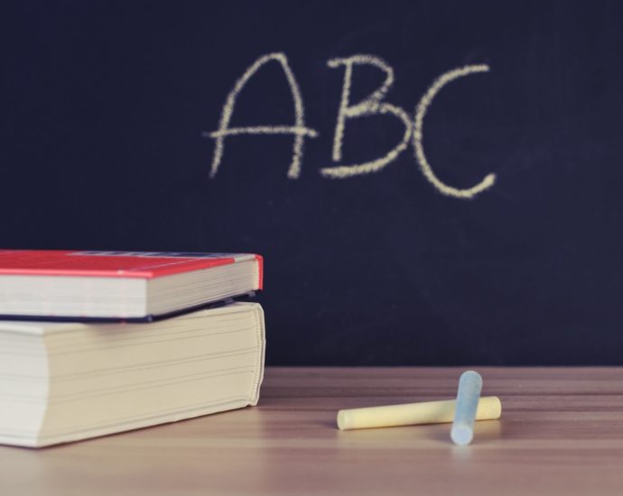 Stack of books and chalk on desk with ABC on blackboard background.